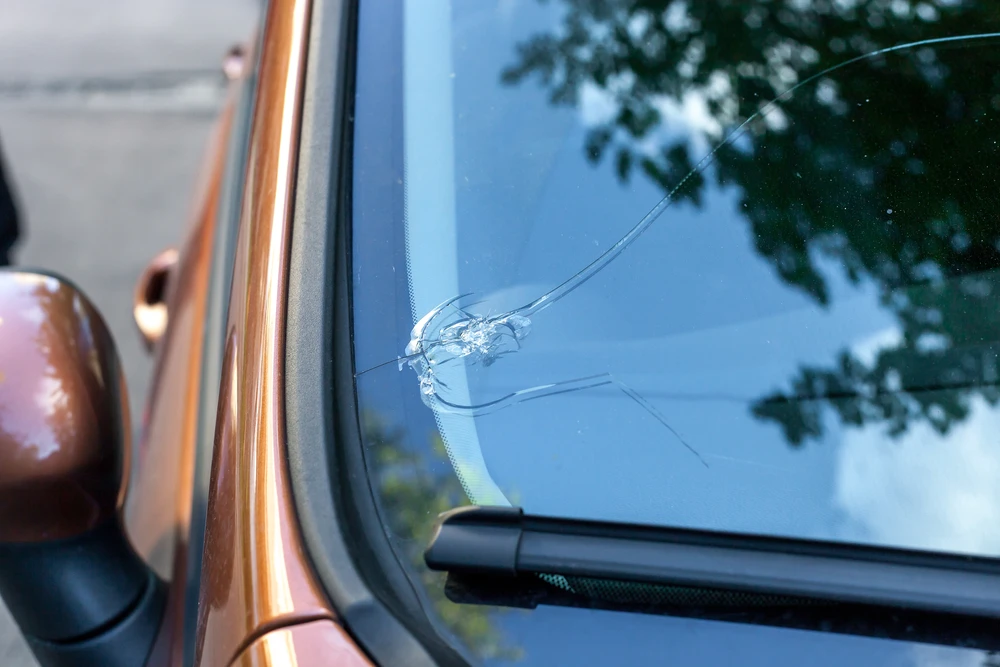 Pare-brise de voiture endommagé avec impact et fissures radiales, véhicule orange garé en extérieur