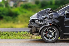 Véhicule accidenté sur route avec dégâts importants à l'avant gauche, carrosserie déformée, pare-chocs détruit