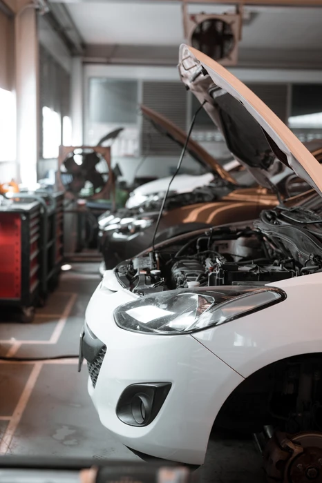 Atelier de réparation automobile avec véhicule blanc, capot ouvert révélant le compartiment moteur