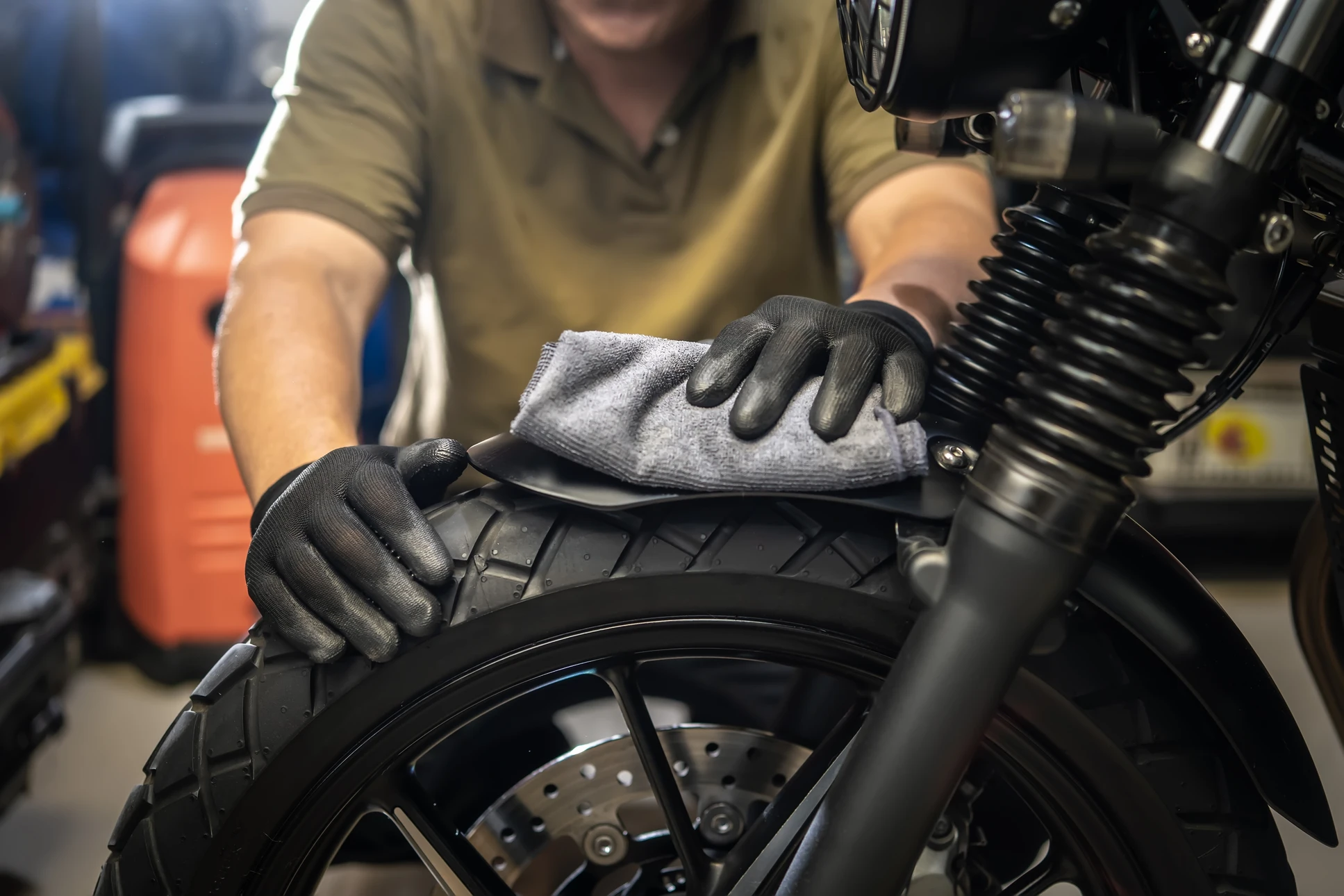 Un mécanicien en salopette kaki nettoie une roue de moto dans un garage automobile