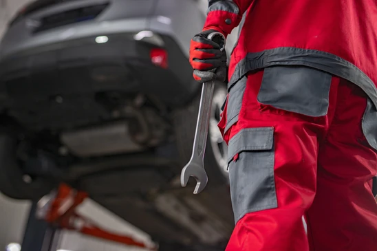 Scène d'intérieur d'atelier de carrosserie professionnelle montrant deux ou trois techniciens qualifiés en train de travailler sur une carrosserie automobile. L'image doit montrer un carrossier ou peintre effectuant des travaux de réparation (débosselage, peinture, ou finitions) dans un environnement d'atelier moderne et bien équipé, avec outils professionnels et équipements visibles. Les techniciens peuvent porter des vêtements de travail ou de protection adaptés. L'atmosphère doit être professionnelle et concentrée, mettant en valeur le savoir-faire et l'expertise métier.