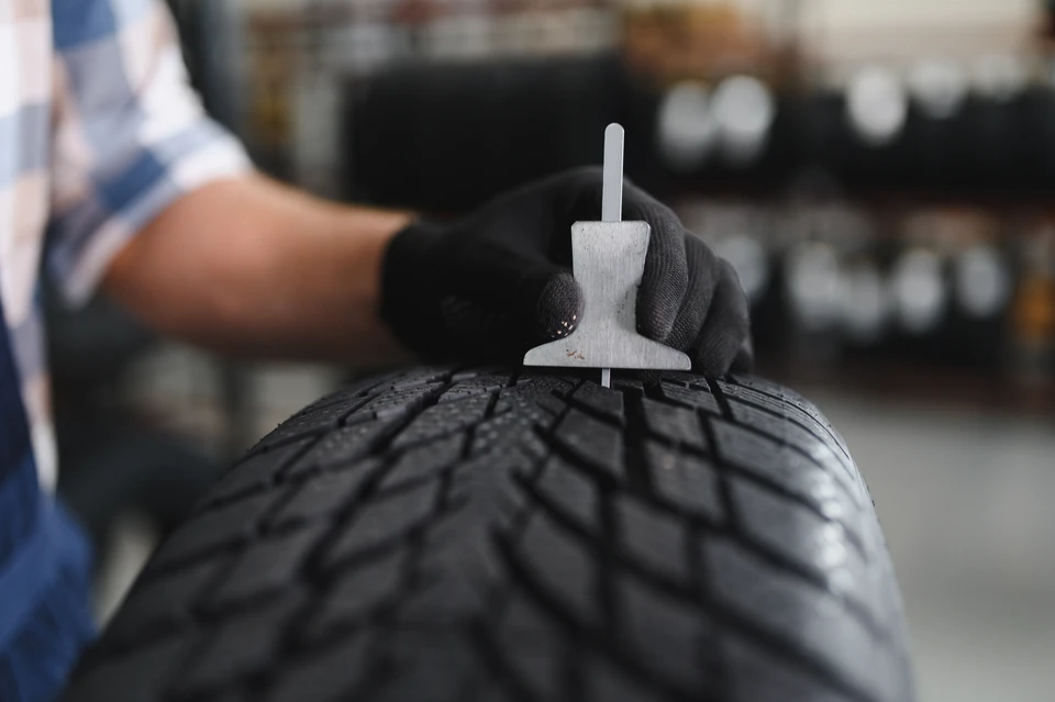 Mécanicien professionnel en combinaison de travail dans un atelier moderne, équipé de matériel spécialisé pour pneumatiques deux-roues, effectuant le montage ou le changement d'un pneu sur une moto. Le mécanicien porte des gants de protection et travaille sur une moto positionnée sur un élévateur ou un stand de maintenance, avec outils pneumatiques et équipement professionnel visibles en arrière-plan.