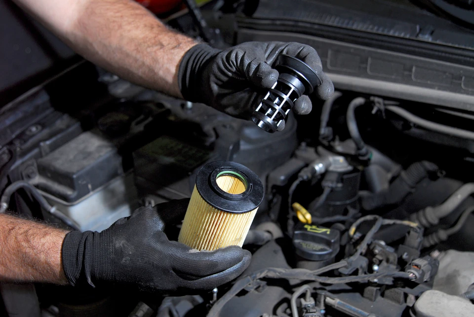 Mécanicien automobile effectuant une maintenance moteur, mains gantées manipulant un filtre à huile cylindrique neuf près du compartiment moteur ouvert