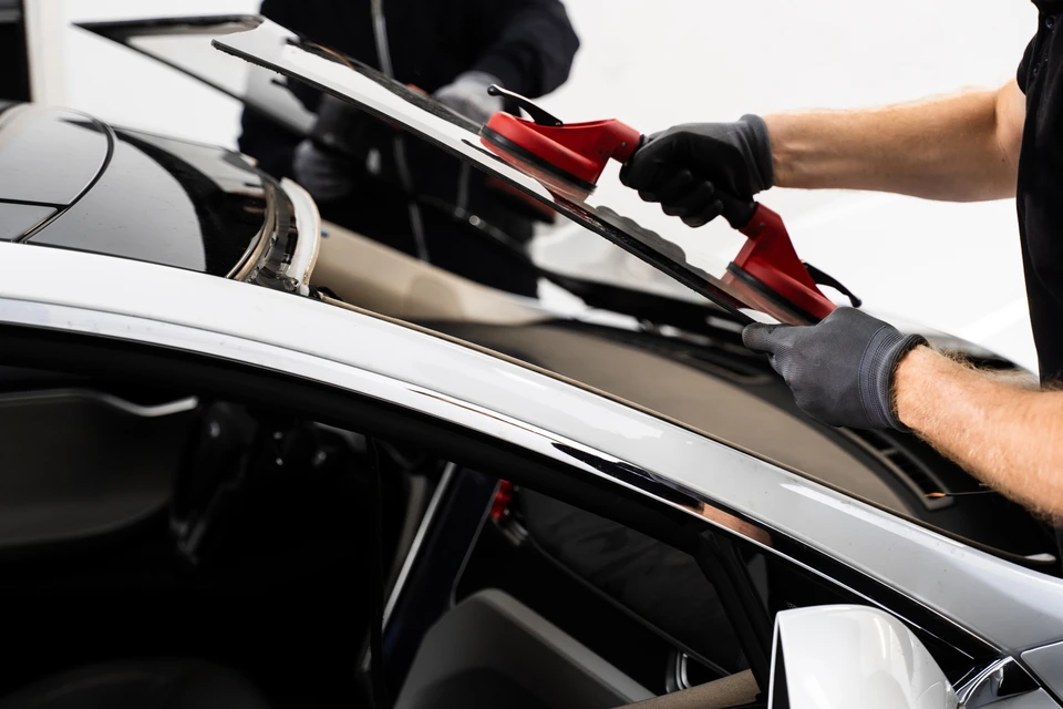 Extérieur, technicien utilisant une ventouse professionnelle bleue pour réparer un pare-brise de véhicule, travail de vitrage automobile sur surface vitrée avec impact visible